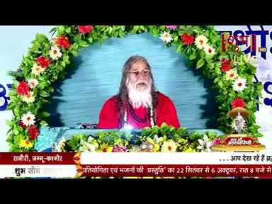 A man with a long white beard and red robes sits centered, framed by a floral archway. The Shubh TV logo is visible, and text at the bottom advertises a presentation of competitions and bhajans.
