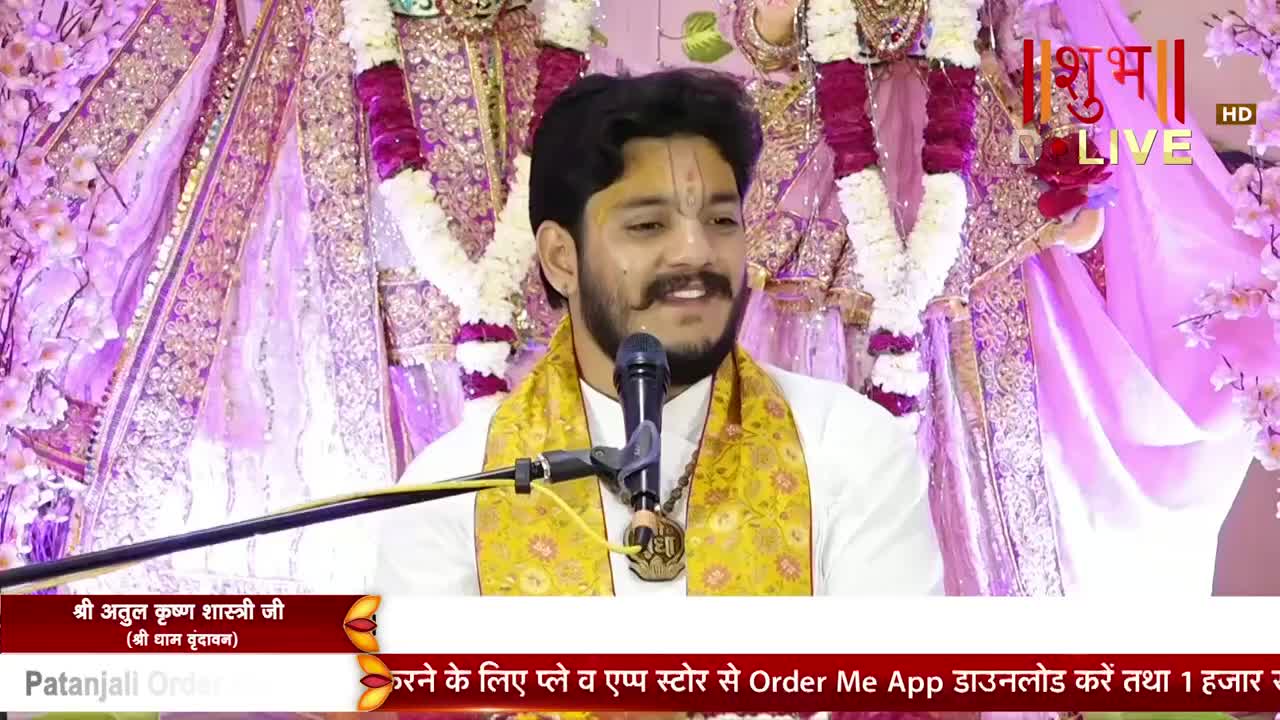 A man with a painted forehead and a microphone is speaking, framed by garlands and ornate drapes. The Shubh TV logo is visible in the upper right corner, and text in Hindi runs along the bottom of the screen.
