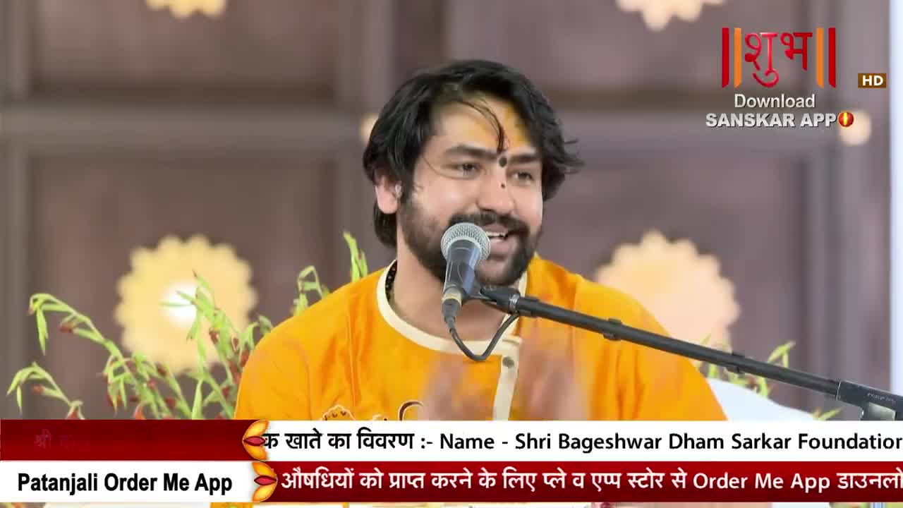 A man in an orange shirt speaks into a microphone, his face lit up as he addresses the audience. The Shubh TV logo is visible in the upper right corner, and the bottom of the screen displays scrolling text in Hindi.
A man in an orange shirt speaks into a microphone, his face lit up as he addresses the audience. The Shubh TV logo is visible in the upper right corner, and the bottom of the screen displays scrolling text in Hindi.