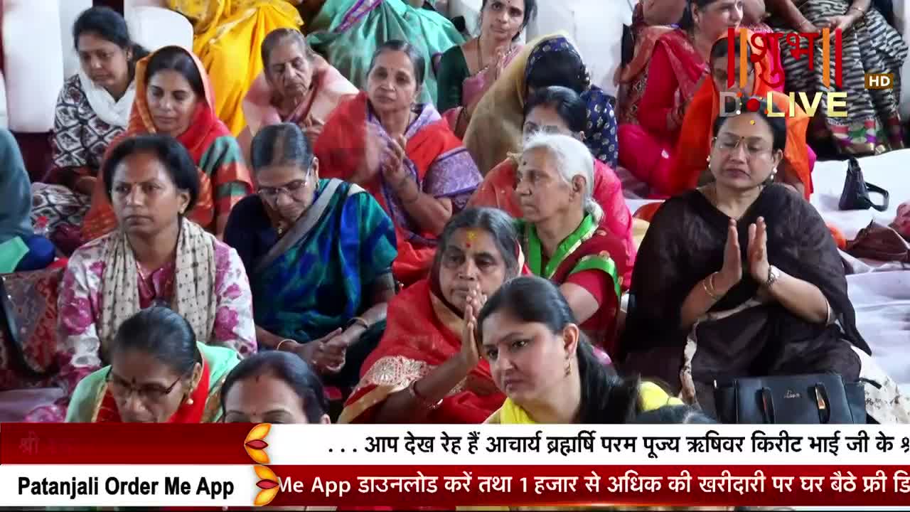 A crowd of women, many in colorful saris, sit closely together, some with hands folded in prayer. The Shubh TV logo is visible, and the broadcast is likely coming from India.
A crowd of women, many in colorful saris, sit closely together, some with hands folded in prayer. The Shubh TV logo is visible, and the broadcast is likely coming from India.