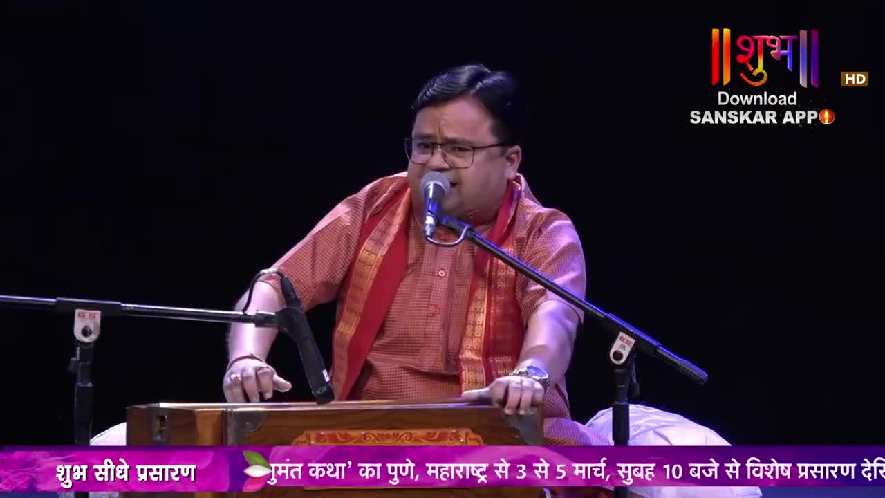 A man in a red kurta sings into a microphone, his hands resting on a harmonium. The Shubh TV logo appears in the corner, advertising a live broadcast.