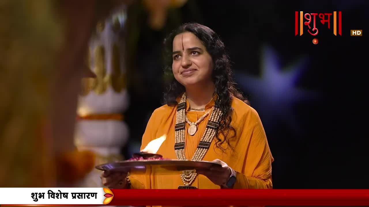 A woman in an orange garment holds a plate with a lit flame, her gaze directed upwards. The Shubh logo is visible in the background.