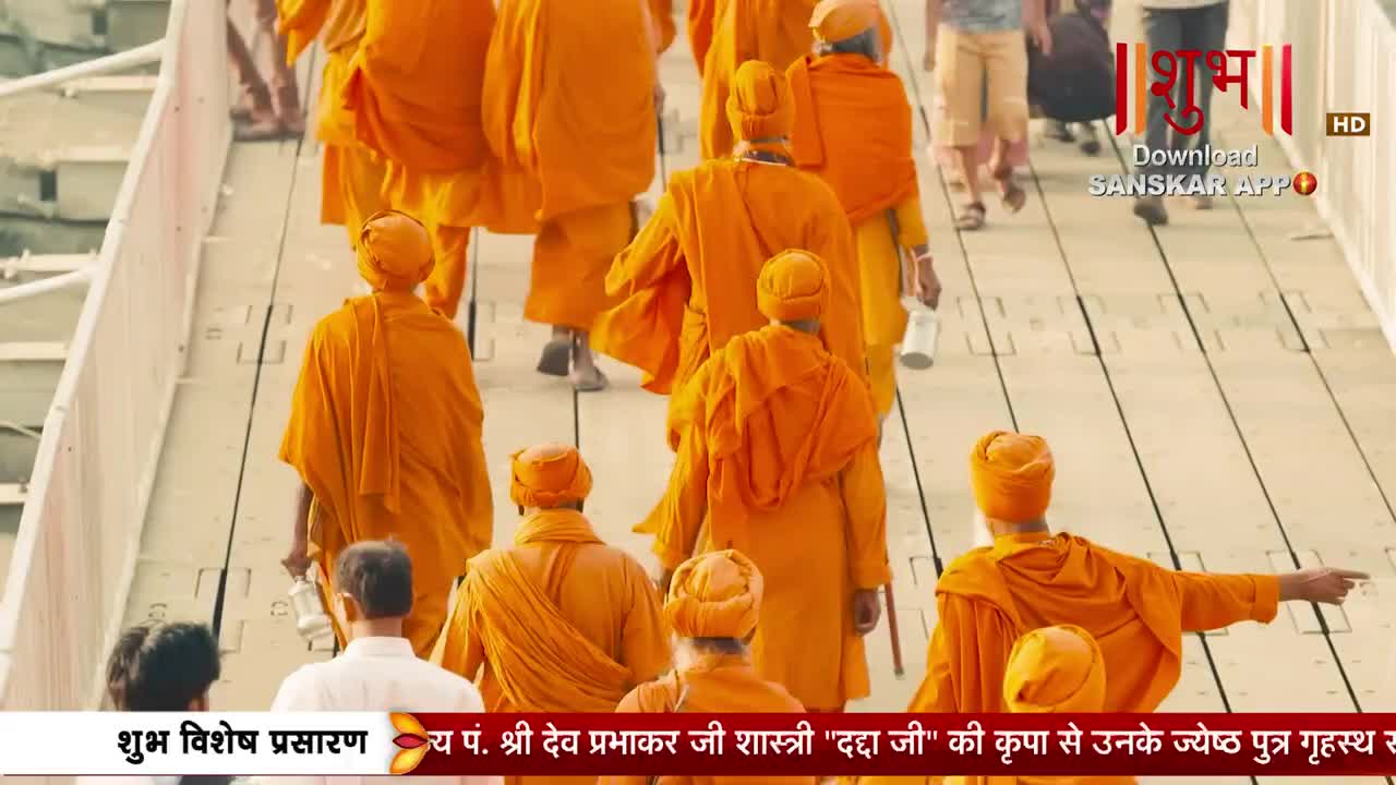 A procession of men in bright orange robes walks across a bridge. Their saffron head coverings match their flowing garments as they move together.