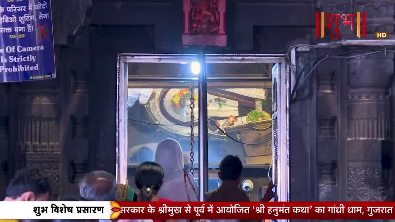 People gather at the entrance of a temple, looking towards an altar. A bright light illuminates the space within, where offerings are visible.