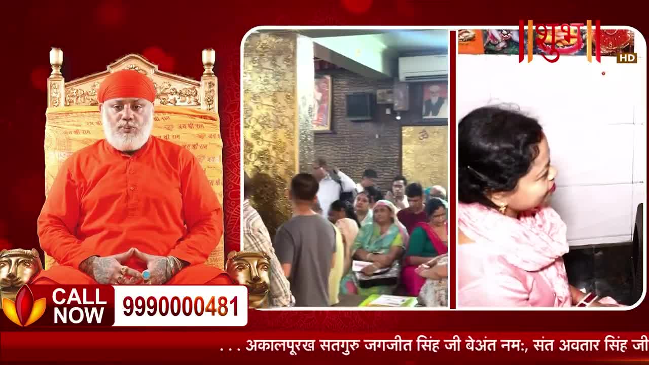 A man in an orange robe sits on a golden throne, his hands clasped. In the background, a crowd of people waits patiently, and a woman looks towards a screen.