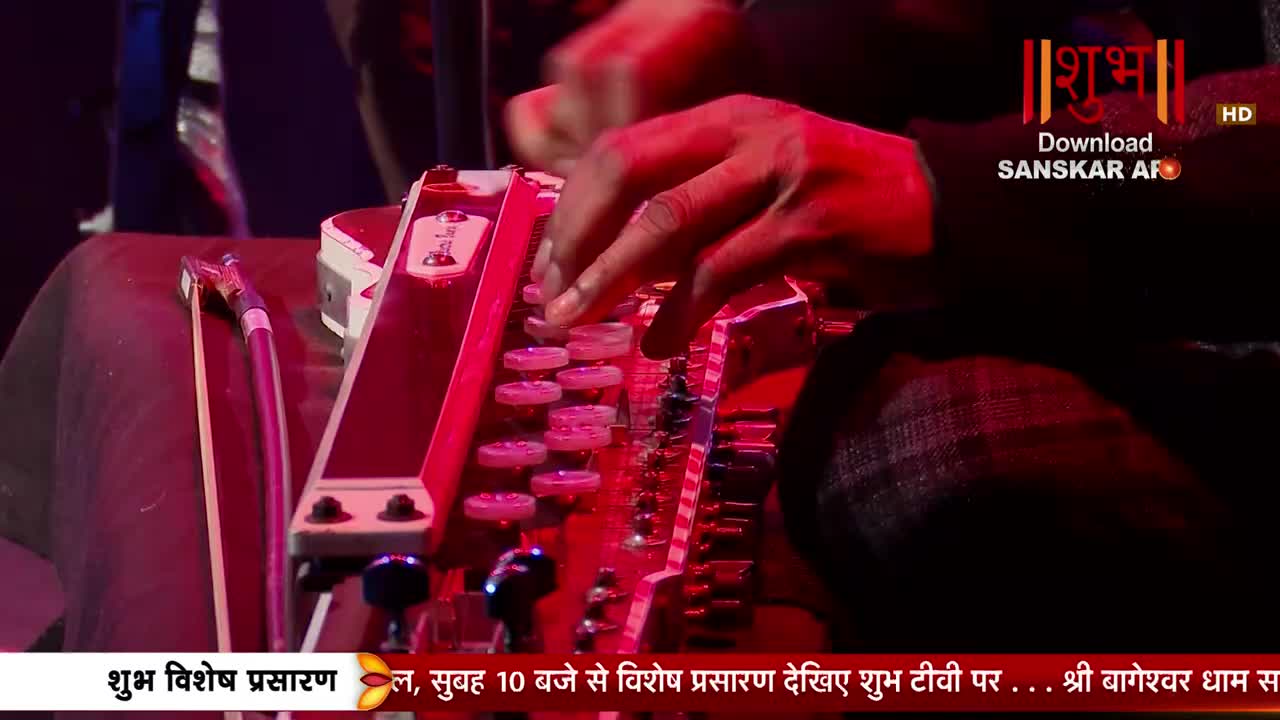 Fingers dance across the keys of a harmonium, its red glow illuminating the performer's hands. A bow rests beside the instrument, hinting at a melody about to unfold.