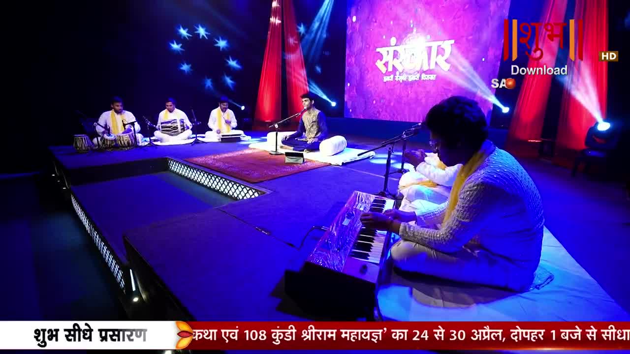 A group of musicians performs on a stage, with one man playing a keyboard while others tap on drums. The backdrop displays the Shubh TV logo and the word "संस्कार" in Hindi.