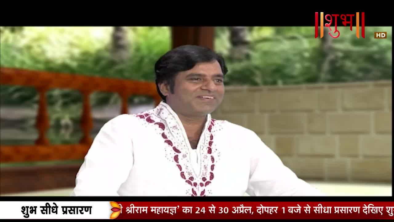 A man in a white kurta with red embroidery smiles at the camera. A banner at the bottom of the screen announces a live broadcast on Shubh TV.
