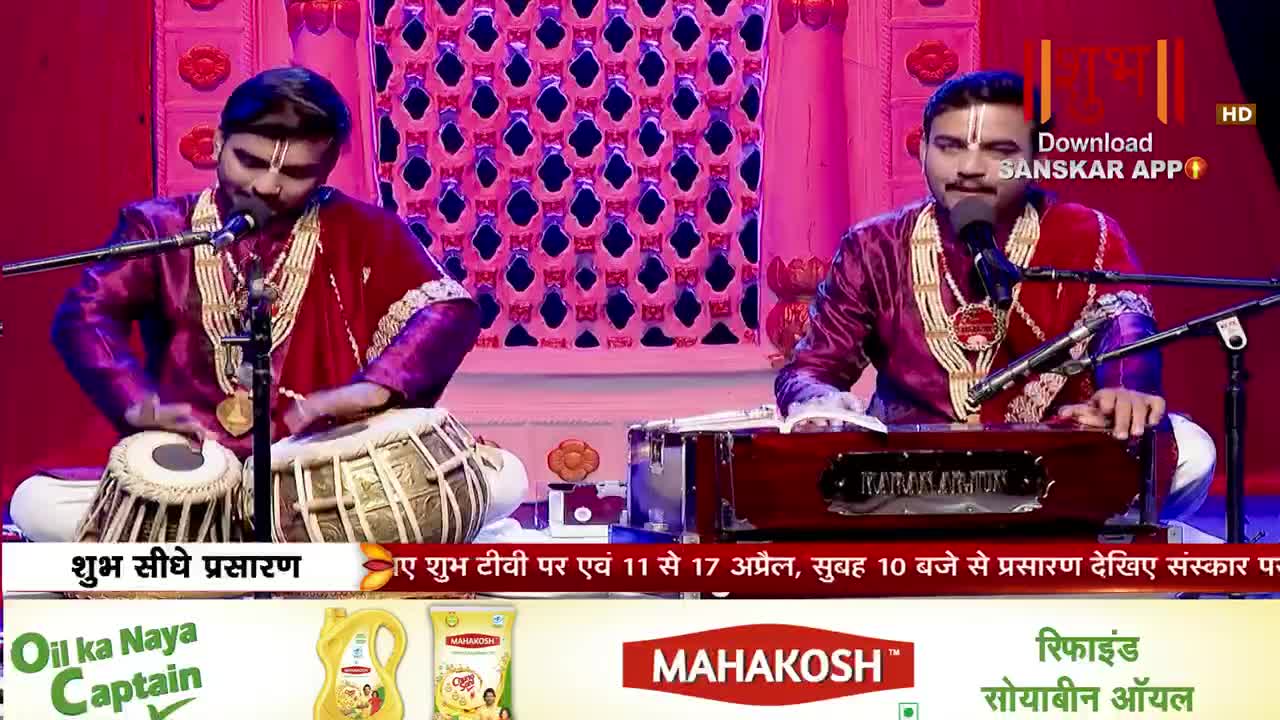A musician plays the tabla with quick, precise movements of his hands. Beside him, another man plays a harmonium, his fingers dancing across the keys.