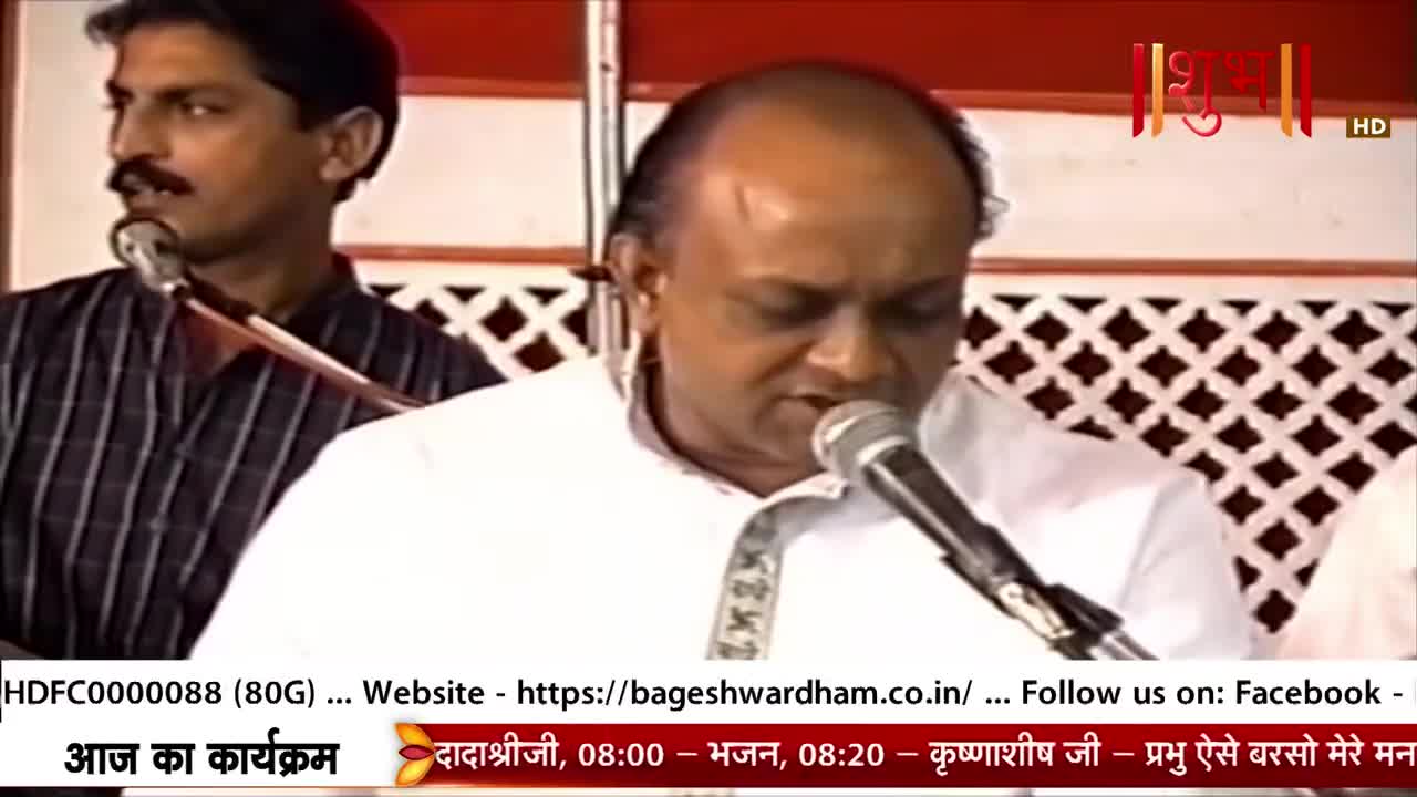 A man in a white shirt speaks into a microphone, his eyes closed. Beside him, another man in a striped shirt also leans towards a mic.