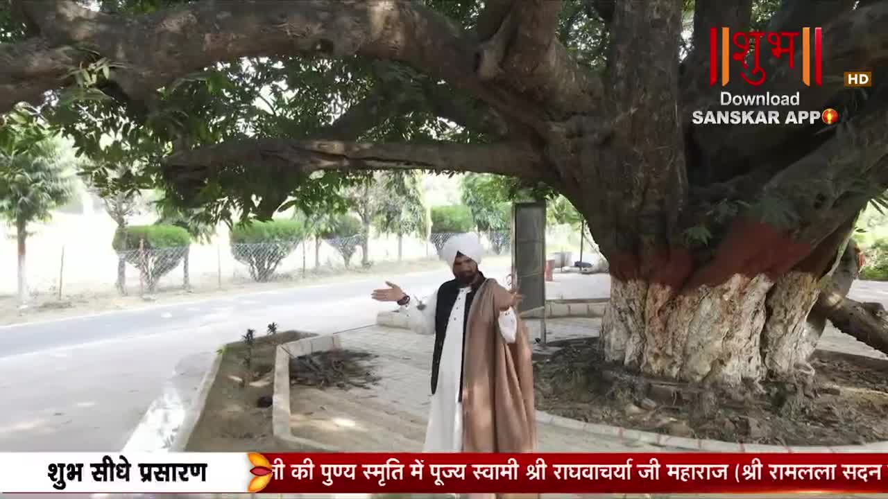 A man in a white turban and traditional Indian attire stands beneath a large tree, gesturing with his hands. The Shubh TV logo appears in the corner, indicating a live broadcast.
