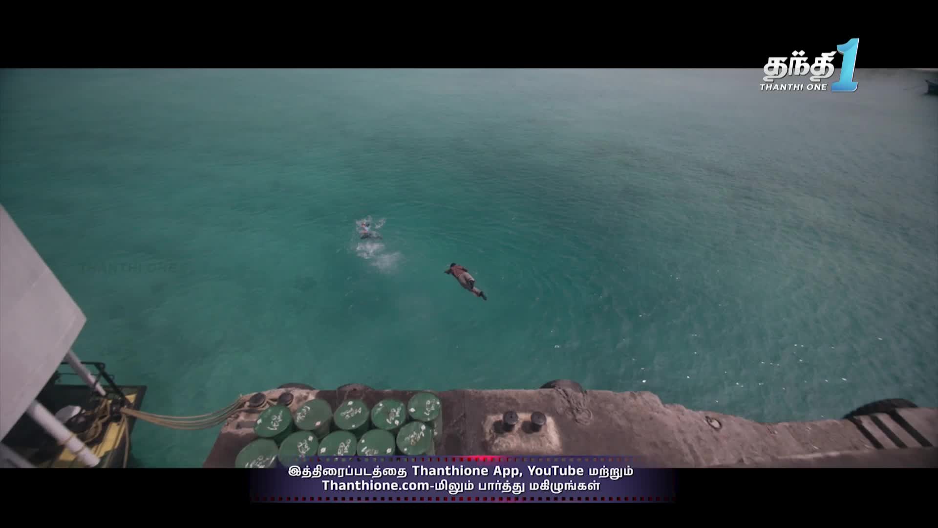 Someone is diving headfirst into the turquoise water, while a swimmer is already in the sea. The scene is being broadcast on Thanthi One, a channel from India.
