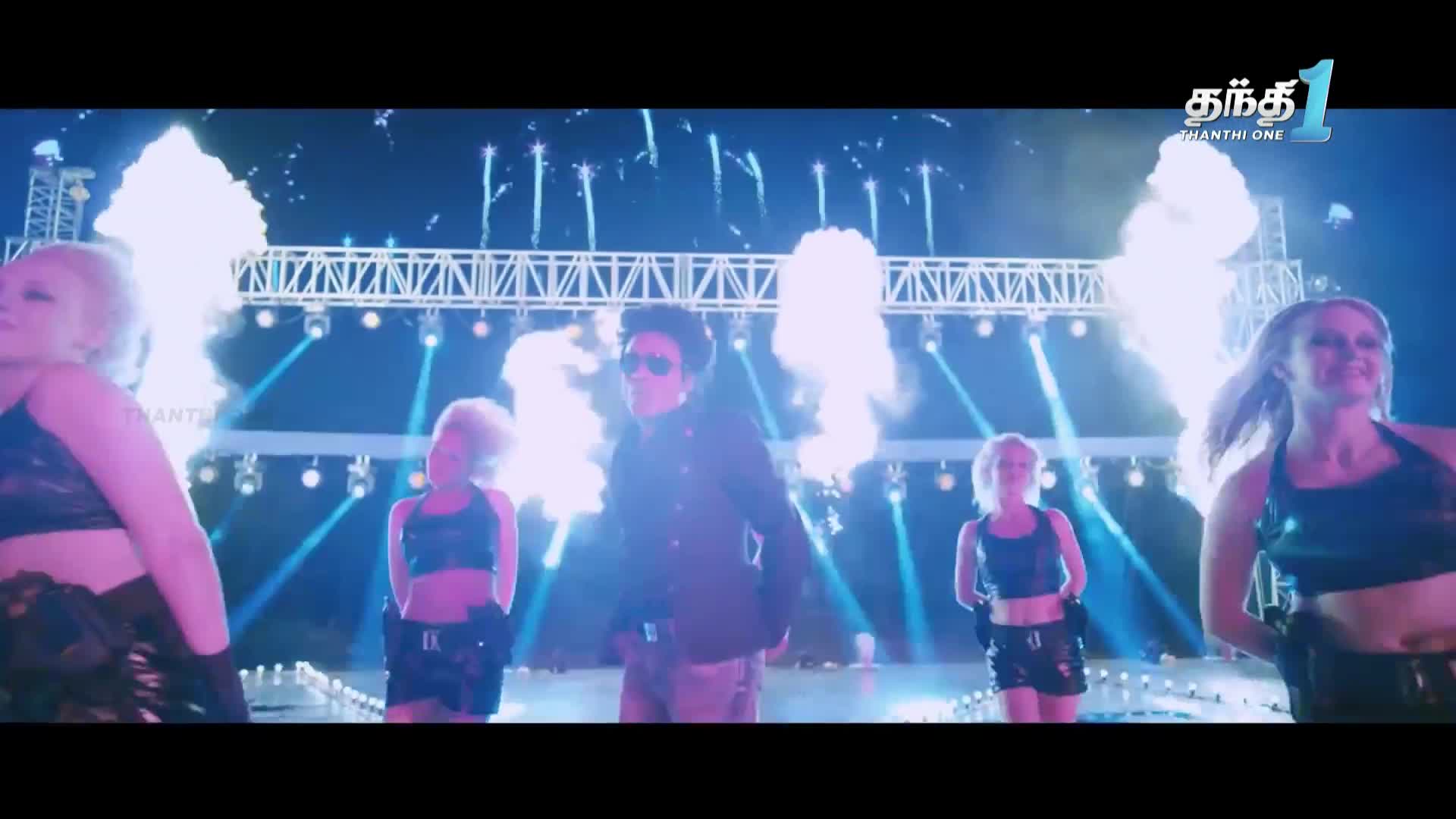 A man in sunglasses stands center stage, flanked by dancers as bursts of smoke erupt behind them. The Thanthi One logo is visible in the corner, and the stage is lit with bright spotlights.
