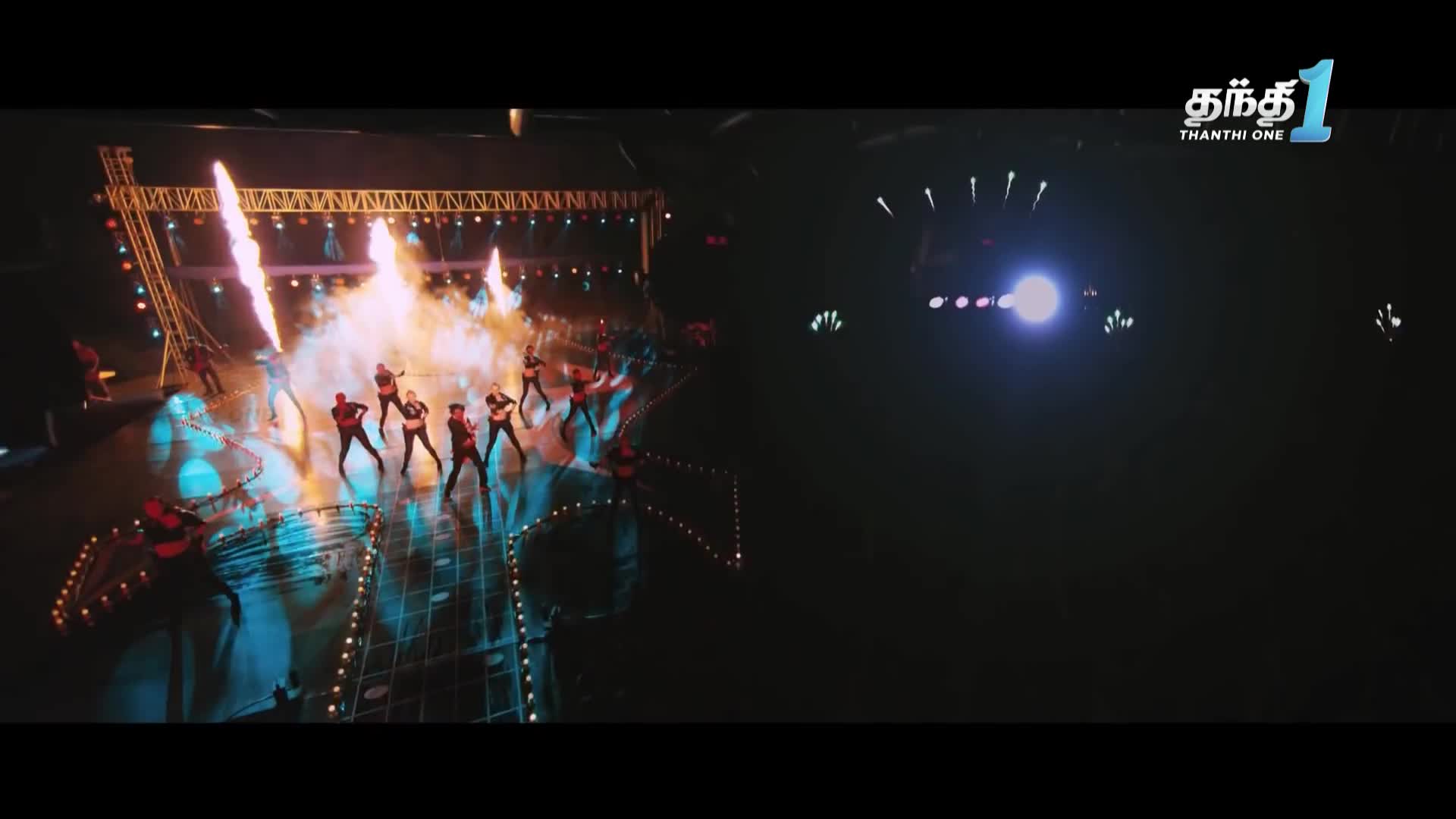 On the stage, a group of musicians in black and red are playing guitars, with flames shooting up behind them. The logo for Thanthi One is visible in the corner.
