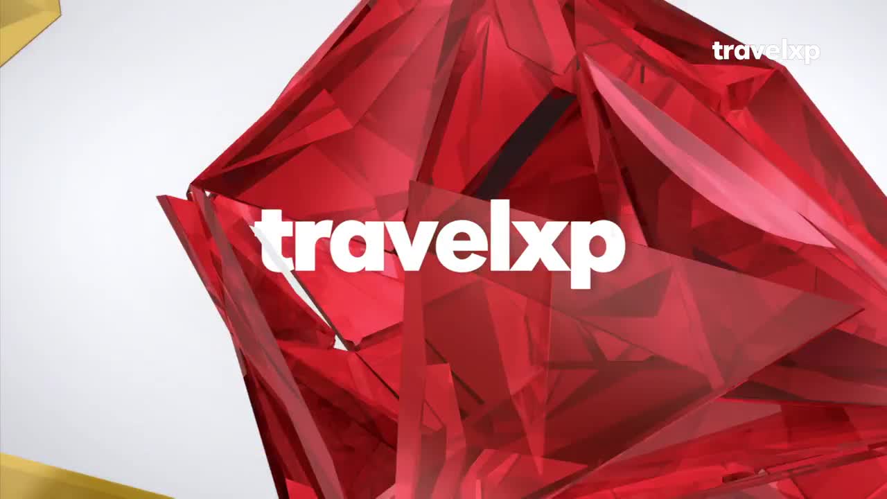 The "travelxp" logo is centered, overlaid on a faceted, red crystal. A geometric shape shifts and sparkles against a white background.
