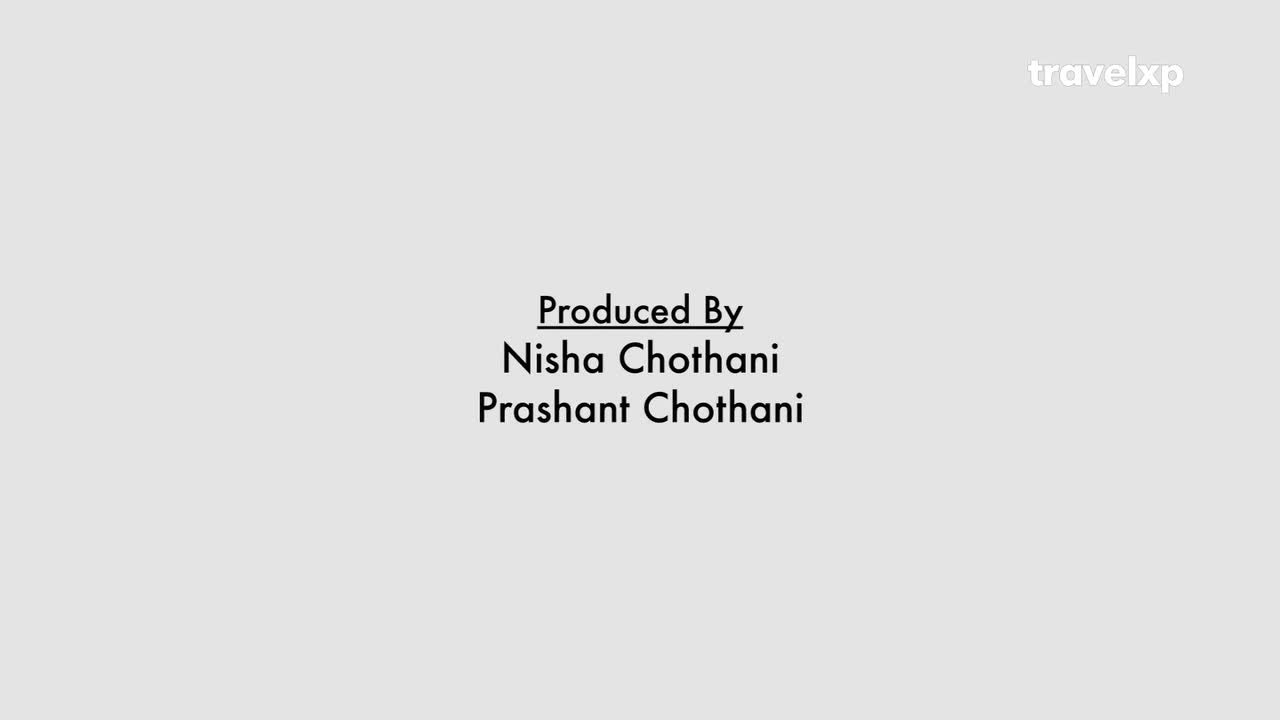 The names of the producers, Nisha Chothani and Prashant Chothani, are displayed in a simple font against a pale background. The Travelxp logo sits in the upper right corner.
