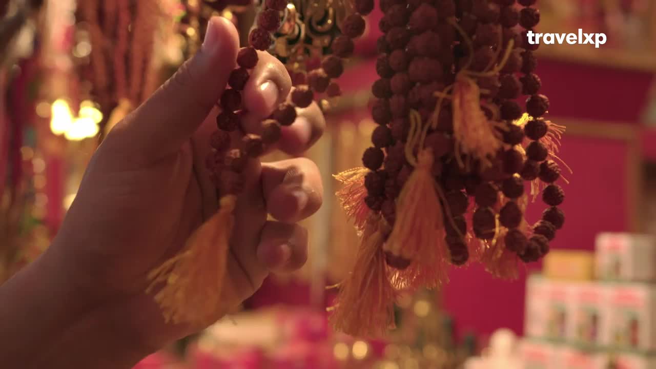 A hand gently holds a strand of brown prayer beads, the small spheres catching the light. The beads hang next to another strand, both with bright yellow tassels.
