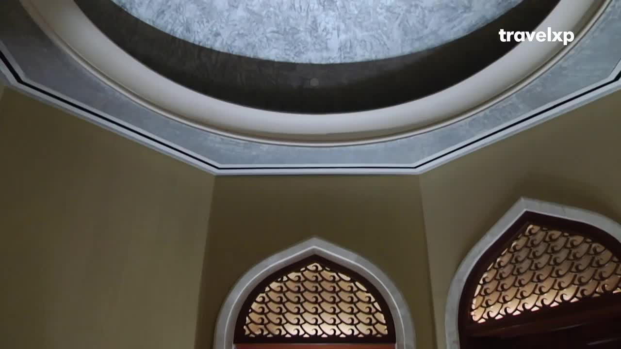 The ornate ceiling curves overhead, its painted details framed by a black line. Below, the arched windows with their intricate, dark wooden screens offer a glimpse of the space beyond.
