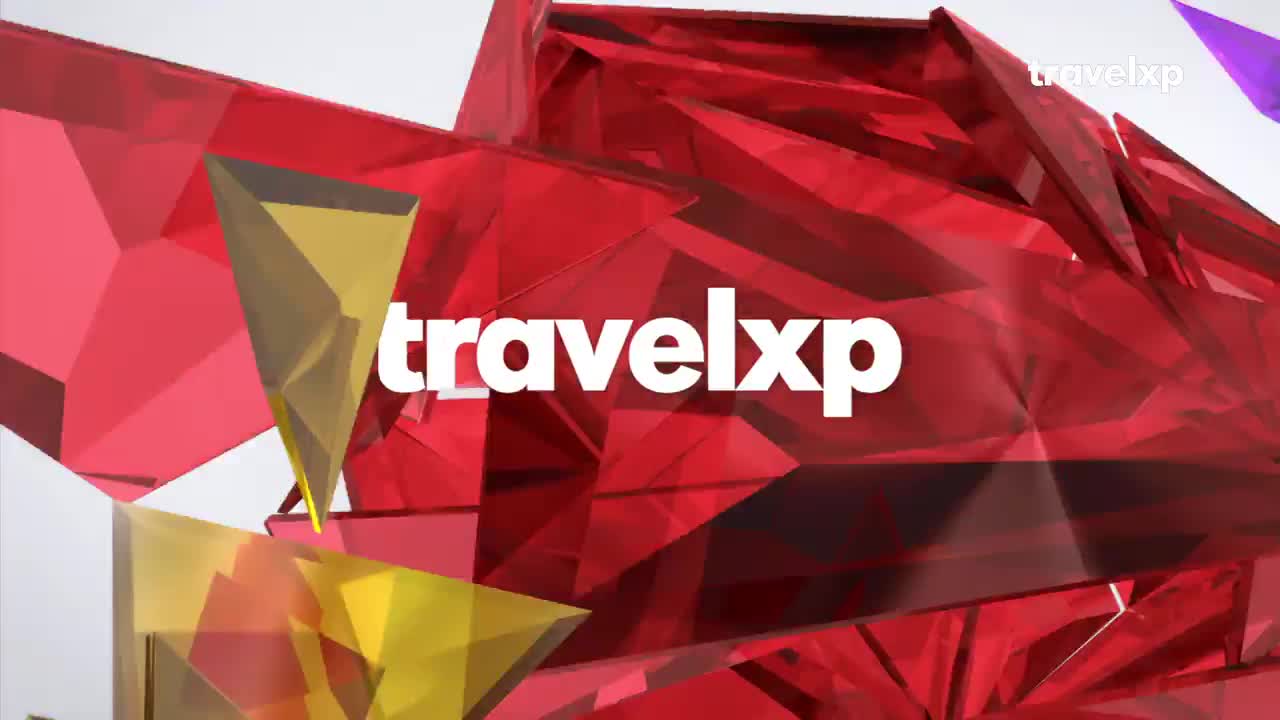 Sharp, faceted shapes of ruby red and amber glass tumble and shift. The word "travelxp" appears in bold white letters against this dynamic backdrop.