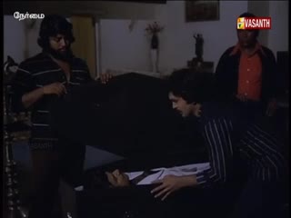 Two men in striped shirts are carefully holding a dark, closed coffin, while another man stands nearby. A Vasanth TV logo is visible, suggesting this is a scene from a show.
