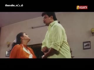 A man in a light green shirt gestures as he speaks to a woman in a bright orange top. The Vasanth TV logo is visible in the corner, suggesting this is a scene from a show.
