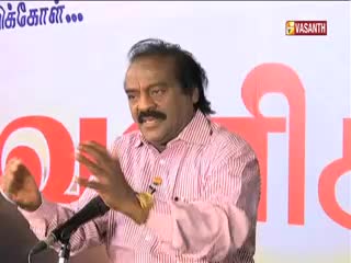 The man in the pink striped shirt gestures with both hands as he speaks into a microphone. A Vasanth TV logo is visible in the upper right corner of the screen.
