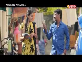 A man in a blue shirt gestures with money in his hand, facing a woman in a yellow dress. They're standing outside, with laundry hanging in the background, probably filming something for Vasanth TV.
