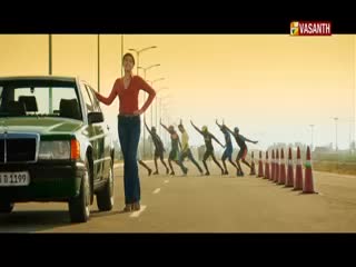 A woman in a red shirt leans against a green car, while a row of runners in various outfits sprint down the road. The Vasanth TV logo is visible in the corner.
