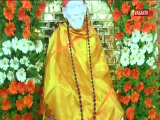 A statue of a figure draped in golden cloth is surrounded by vibrant flowers. The Vasanth TV logo sits in the top right corner, broadcasting from India.
