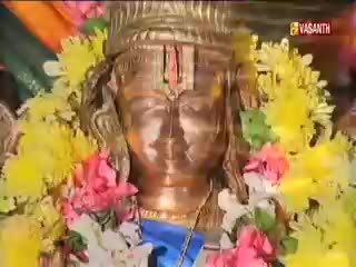 A golden idol, adorned with garlands of yellow and pink flowers, is the focus. The Vasanth TV logo is visible in the top right corner, likely capturing a religious ceremony.
