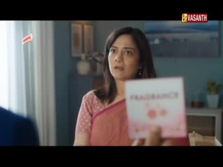 A woman in a pink sari looks at a card someone's holding up, the word "FRAGRANCE" visible. The Vasanth TV logo sits in the corner, and the scene feels like a commercial.
