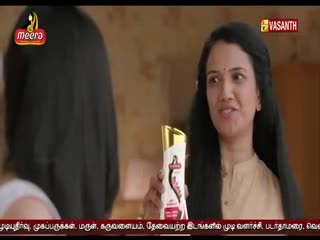A woman on Vasanth TV holds up a bottle of Meera shampoo, talking to someone off-screen. Her dark hair frames her face as she gestures with the product.
