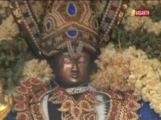 A statue, adorned with elaborate jewels and garlands, is the focus of the Vasanth TV broadcast. The camera is close, highlighting the details of the statue's ornate headwear.
