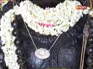 A garland of white flowers rests on a dark, textured surface, with a pendant hanging from a delicate chain. The Vasanth TV logo is visible in the corner, likely broadcasting a religious ceremony from India.
