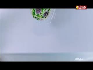 A green and purple object is suspended in the air, seemingly falling. The scene is from Vasanth TV, and the background is a light, neutral color.
