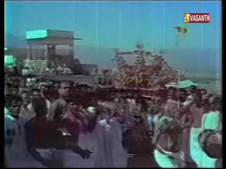 A large crowd is gathered, with many people wearing white, and a structure with a green top stands in the distance. The Vasanth TV logo is visible in the upper right corner, suggesting a broadcast is underway.
