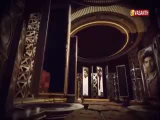 A dark stage with a circular backdrop frames several portrait-like images.  The Vasanth TV logo sits in the corner, and the scene looks like it's from a show in India.
