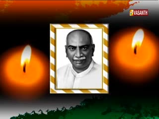 On Vasanth TV, a framed portrait of a man is flanked by two glowing candles, their flames flickering gently. Below, the colors of the Indian flag are subtly displayed.
