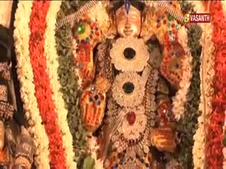 A golden-faced idol is adorned with elaborate jewelry and surrounded by garlands of flowers. The Vasanth TV logo is visible in the corner, broadcasting from India.
