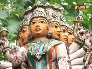 A vibrant, multi-faced statue, likely a deity, stands out against a backdrop of green foliage. The Vasanth TV logo is visible in the corner, suggesting this is part of a broadcast from India.
