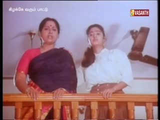 Two women stand behind a wooden railing, looking directly at the camera on what appears to be a Vasanth TV show from India. The woman on the left wears a red blouse and a dark blue sari, while the other is in a white shirt.

