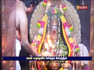 A man in India, on what looks like Vasanth TV, is tending to a flame in front of a decorated shrine. The flickering light illuminates the ornate structure and the man's focused expression.
