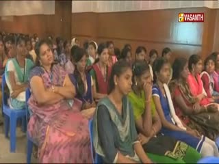 A large group of women sit in rows of blue chairs, many with their arms crossed or hands on their faces. The Vasanth TV logo is visible in the corner.
