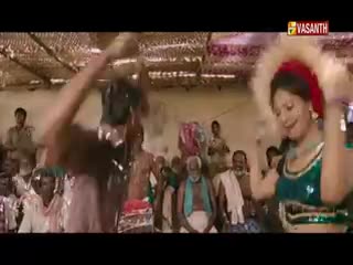 A woman in a green top and a red headscarf dances energetically, her arms raised. Overhead, the Vasanth TV logo marks the broadcast from India, and a crowd watches the performance.
