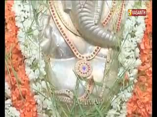 A garland of white and orange flowers frames a statue of a deity, likely in India. The Vasanth TV logo is visible in the corner, indicating a broadcast of the ceremony.
