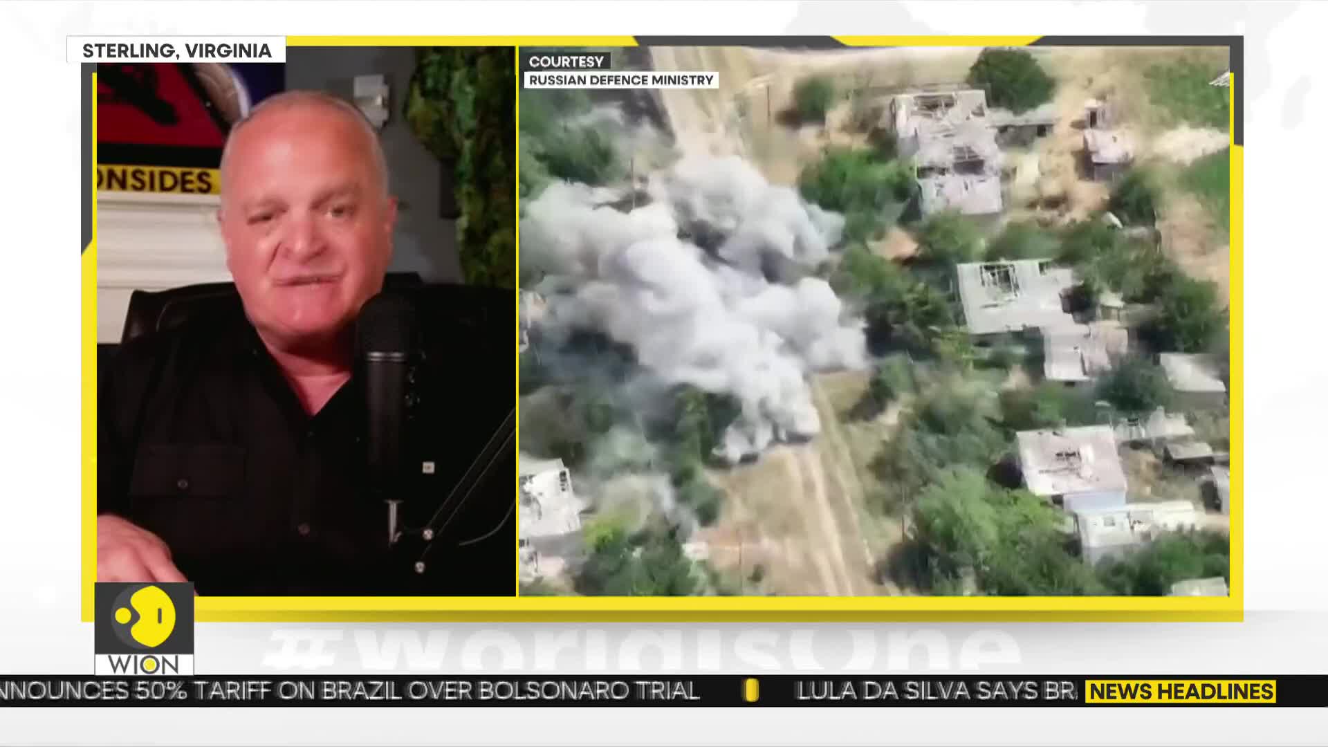 A man in a black shirt is speaking into a microphone, framed by a yellow border. On the right, a plume of smoke billows over a cluster of buildings, likely from an aerial view.

