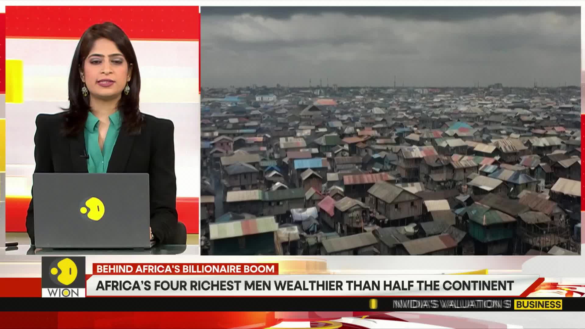 A news anchor from WION in India is seated behind a desk, looking directly at the camera. Behind her, a densely packed settlement of small, mismatched houses stretches into the distance under a cloudy sky.
