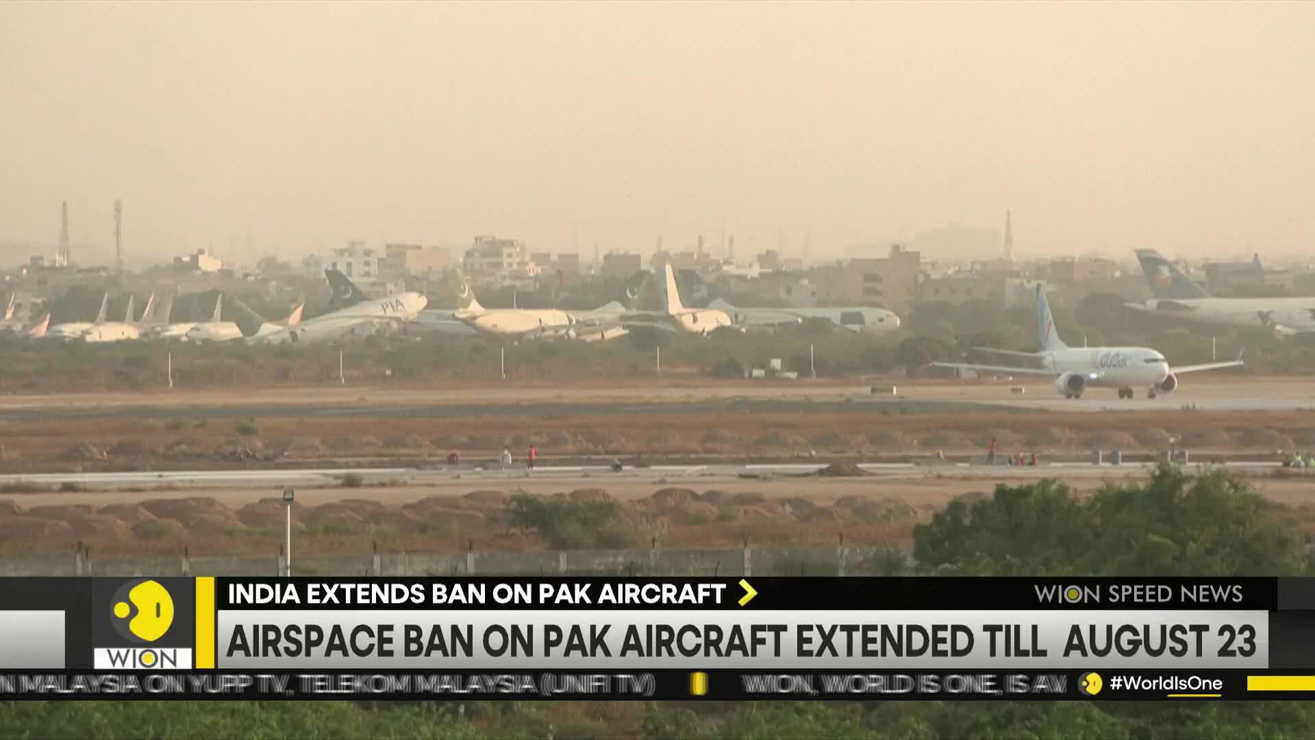 A plane is taxiing on the runway, while several other aircraft sit parked in the distance. The news ticker from WION reports India's extended airspace ban.
