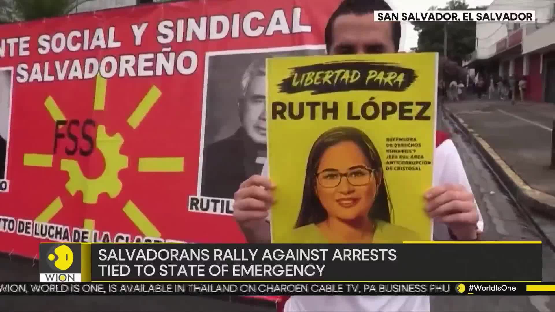 A man holds a sign with a portrait and the words "Libertad Para Ruth Lopez" in front of a large red banner. Other protesters are visible in the background, and the WION logo is in the bottom left corner.

