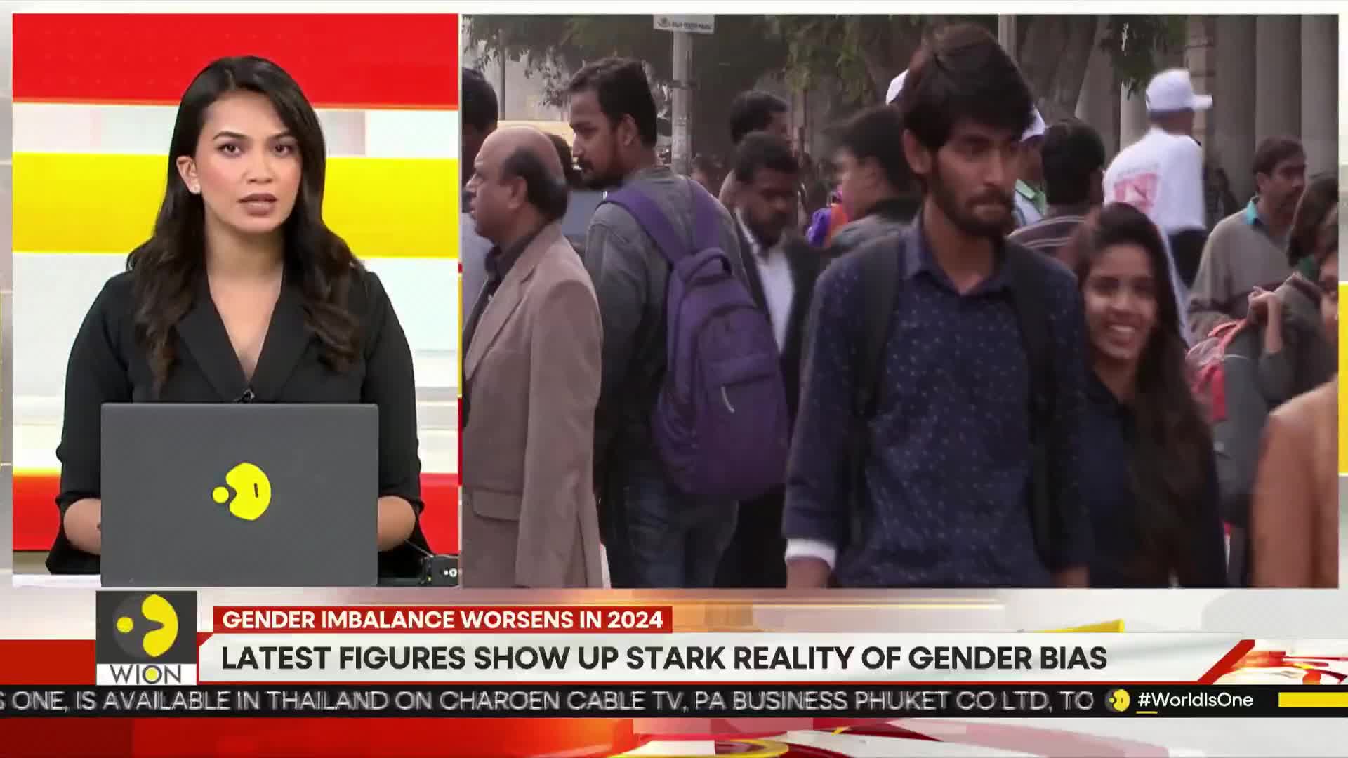 A news anchor on WION in India is reporting on a laptop, while a street scene plays on the screen behind her. People are walking past in the background, some looking at the camera.
